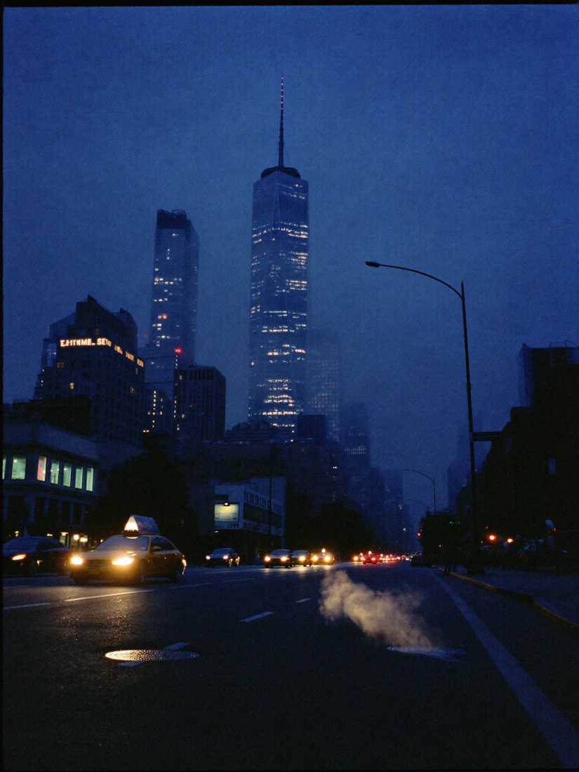 A taxi on a New York avenue below One World Trade Center at dusk