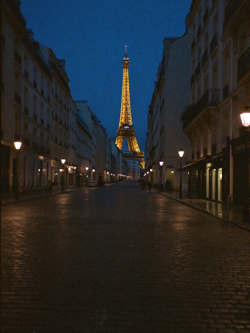 The Eiffel Tower lit at dusk at the end of a Paris street
