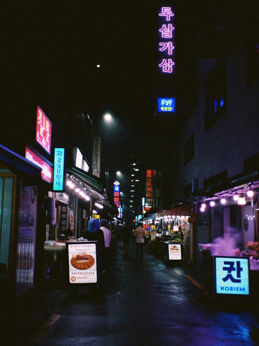 Neon-lit food alley in Seoul at night after rain