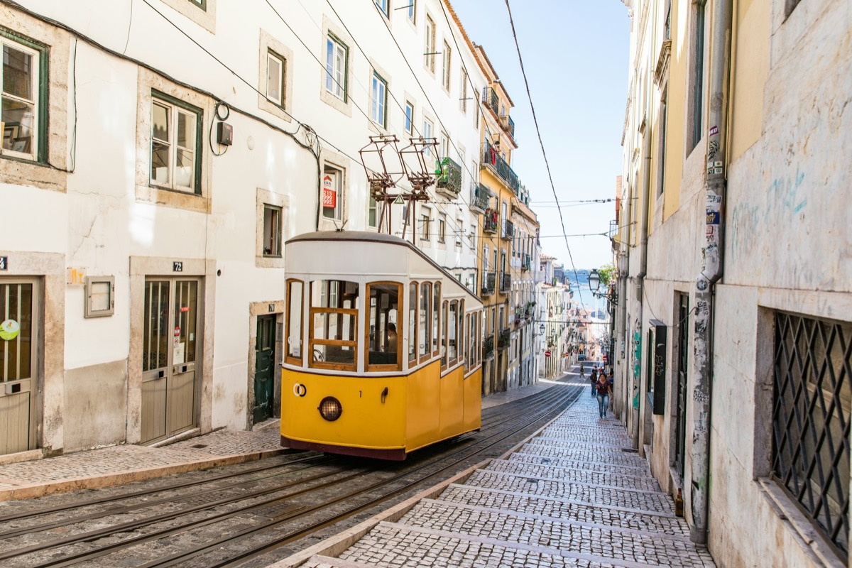 A yellow tram on a steep Lisbon street in daylight
